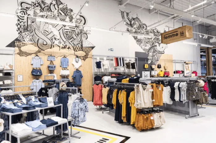 Intérieur d’un magasin de mode Gémo : rayon femme, portants et fresque murale